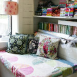 A cozy nook features three Tula Pink needlepoint pillows.