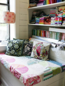 A cozy nook features three Tula Pink needlepoint pillows.