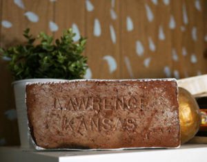 A brick stamped Lawrence, Kansas sits on a bookcase in Seth Smith's studio.