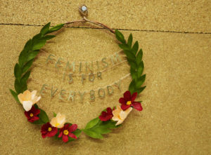 A floral wreath proclaims "feminism is for everybody", made by Grace D. Chin.