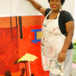 Glyneisha stands next to her current work in progress, a bright red collage based on a scene from the movie Do The Right Thing.