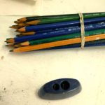 A bundle of drawing pencils sit next to a sharpener and eraser.