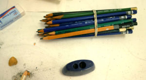 A bundle of drawing pencils sit next to a sharpener and eraser.